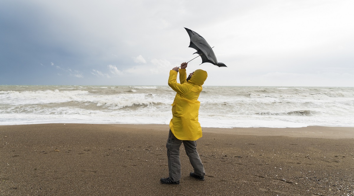Homme sur une plage avec une veste de pluie jaune tenant son parapluie dans le vent