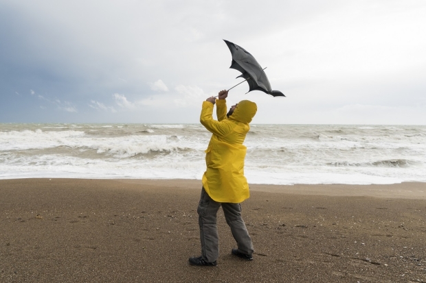 Man at the beach with a yellow rain jacket holding on to his umbrella in the wind